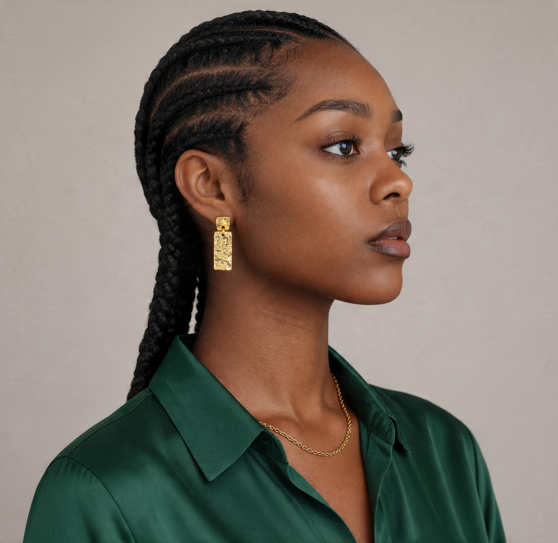 CameroonJewels Les Piliers square-cut gold-plated stud earrings worn by a woman in a green shirt